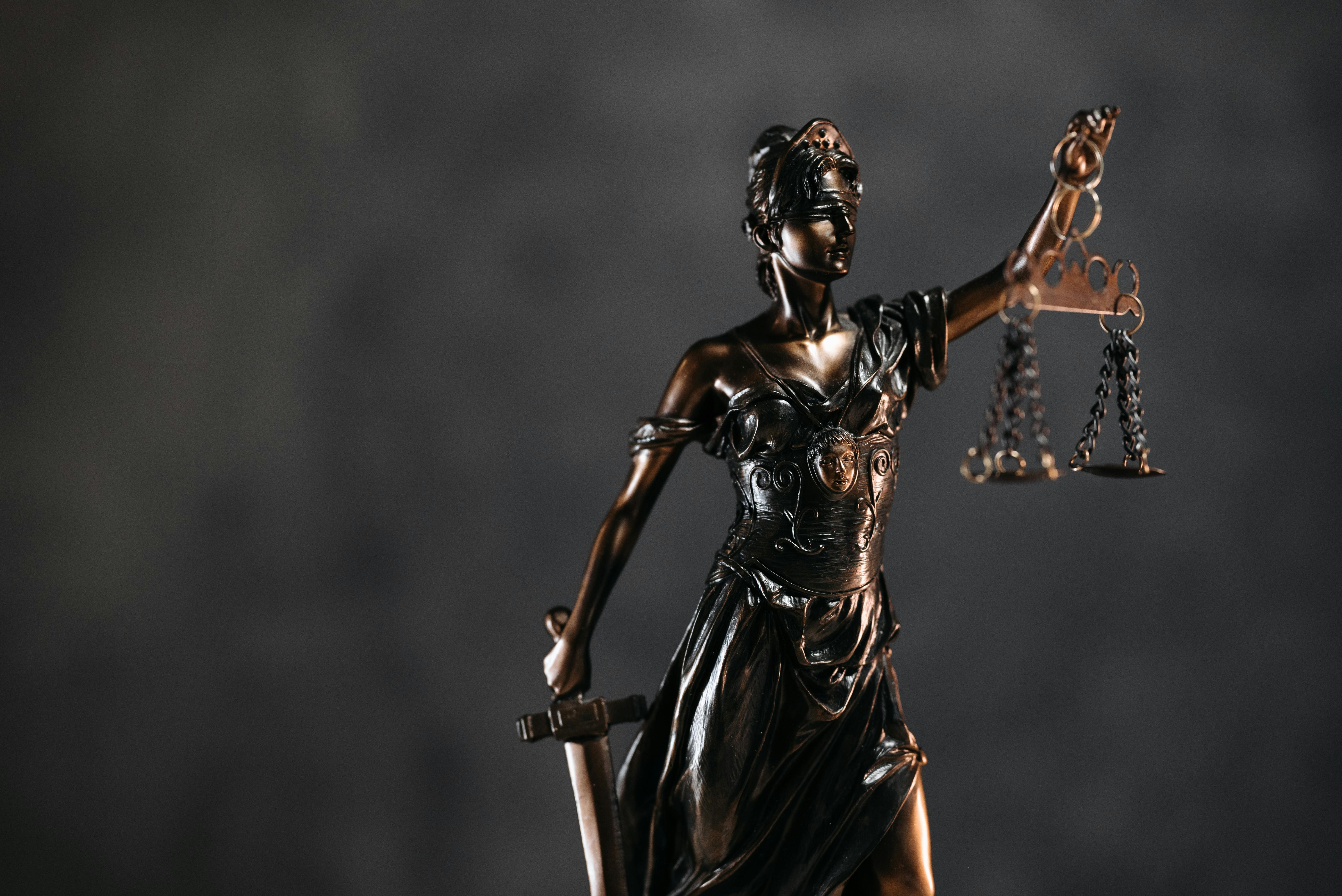 Detailed bronze Lady Justice statue with scales and sword against a dark background, symbolizing law and justice.